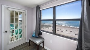 Une pièce dotée d’une grande fenêtre donnant sur une plage, d’une porte avec des stores et d’un banc agrémenté d’un coussin.