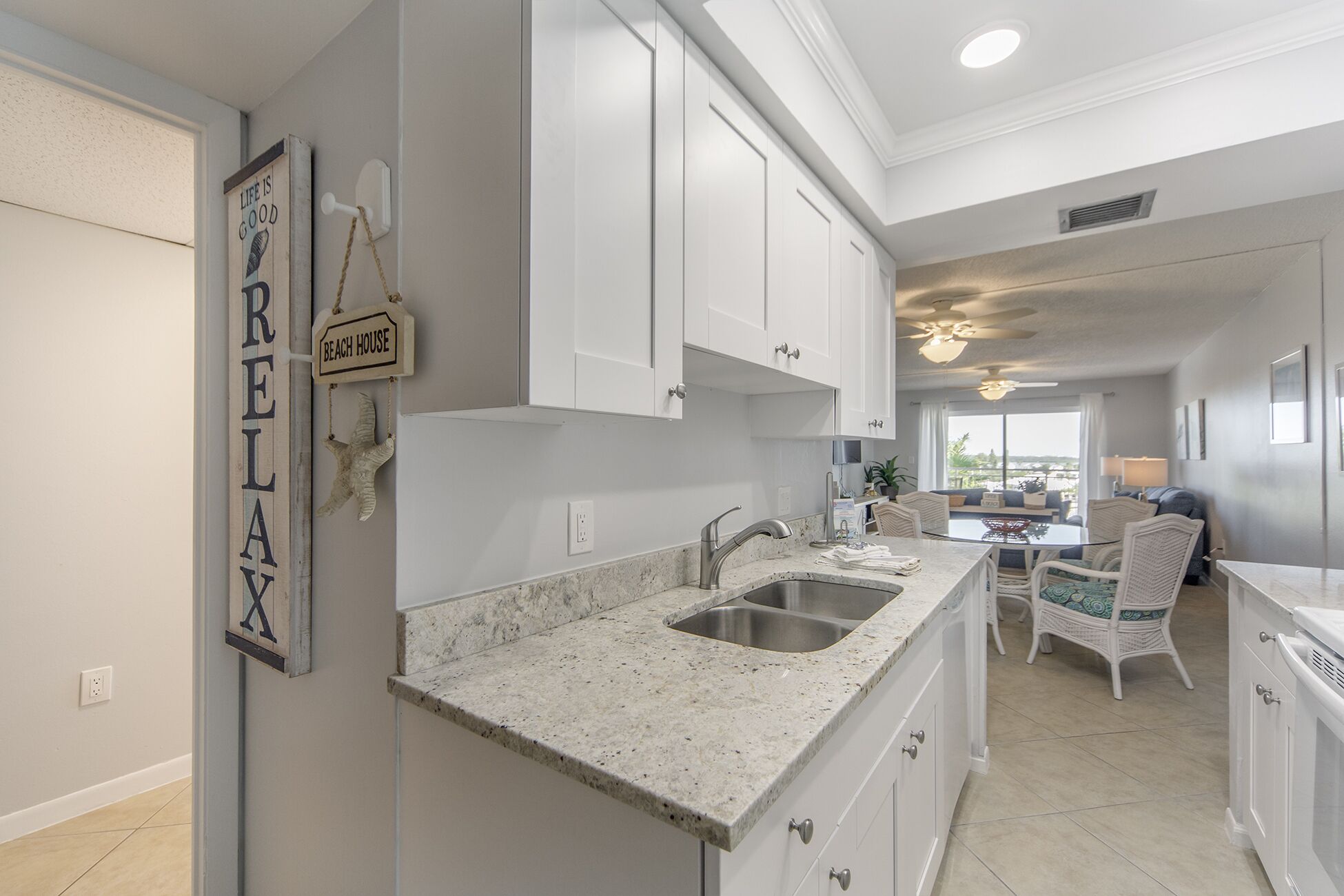 A kitchen with white cabinets, granite countertops, and a dining area with wicker chairs.