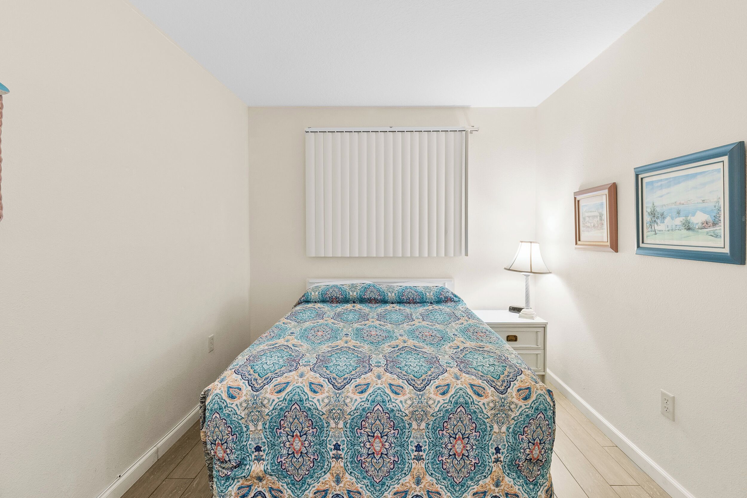 Un dormitorio con una cama, una mesita de noche, una lámpara y una ventana con persianas.