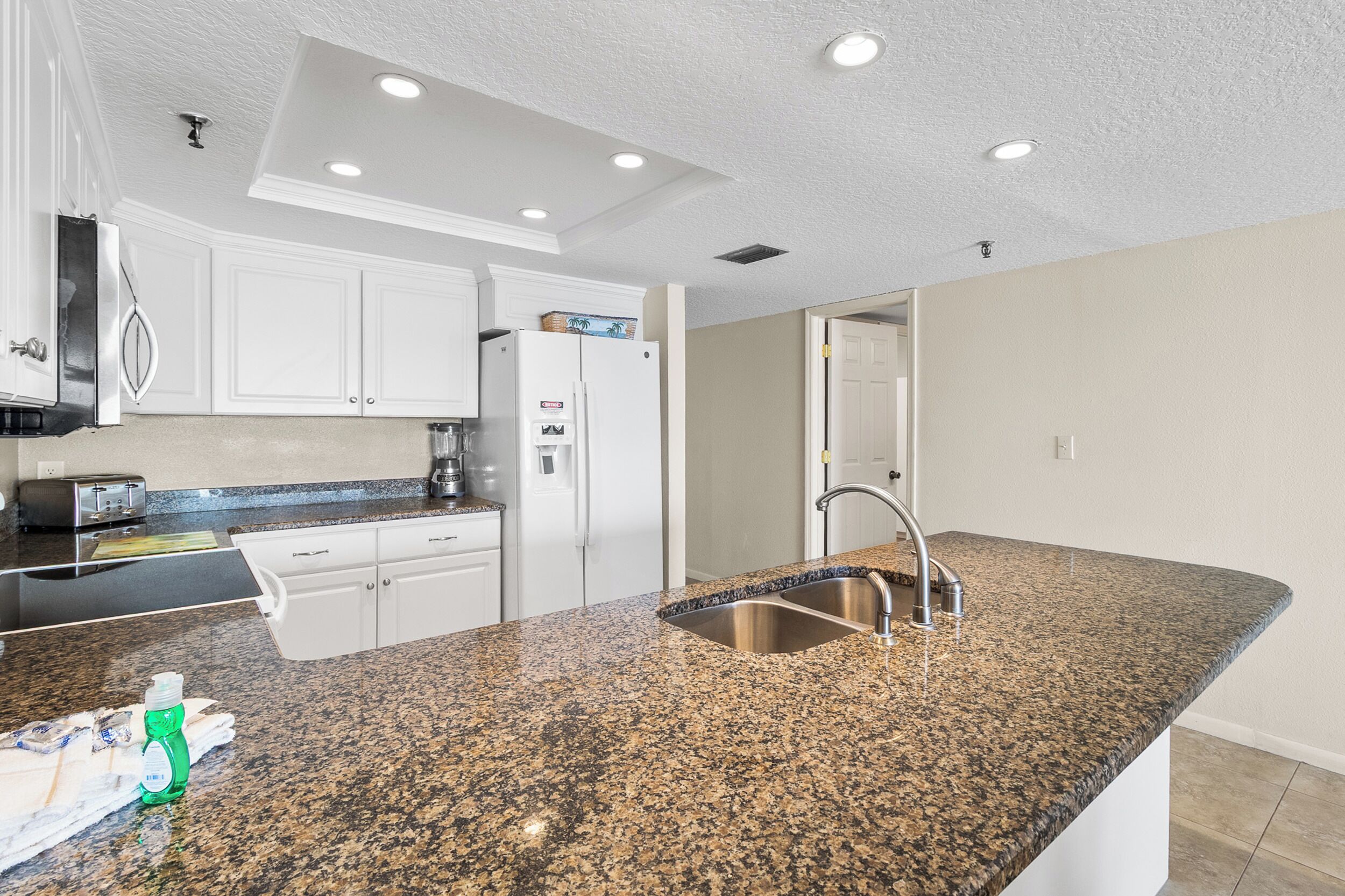 A kitchen with white cabinets, a granite countertop, a stainless steel sink, and a refrigerator.
