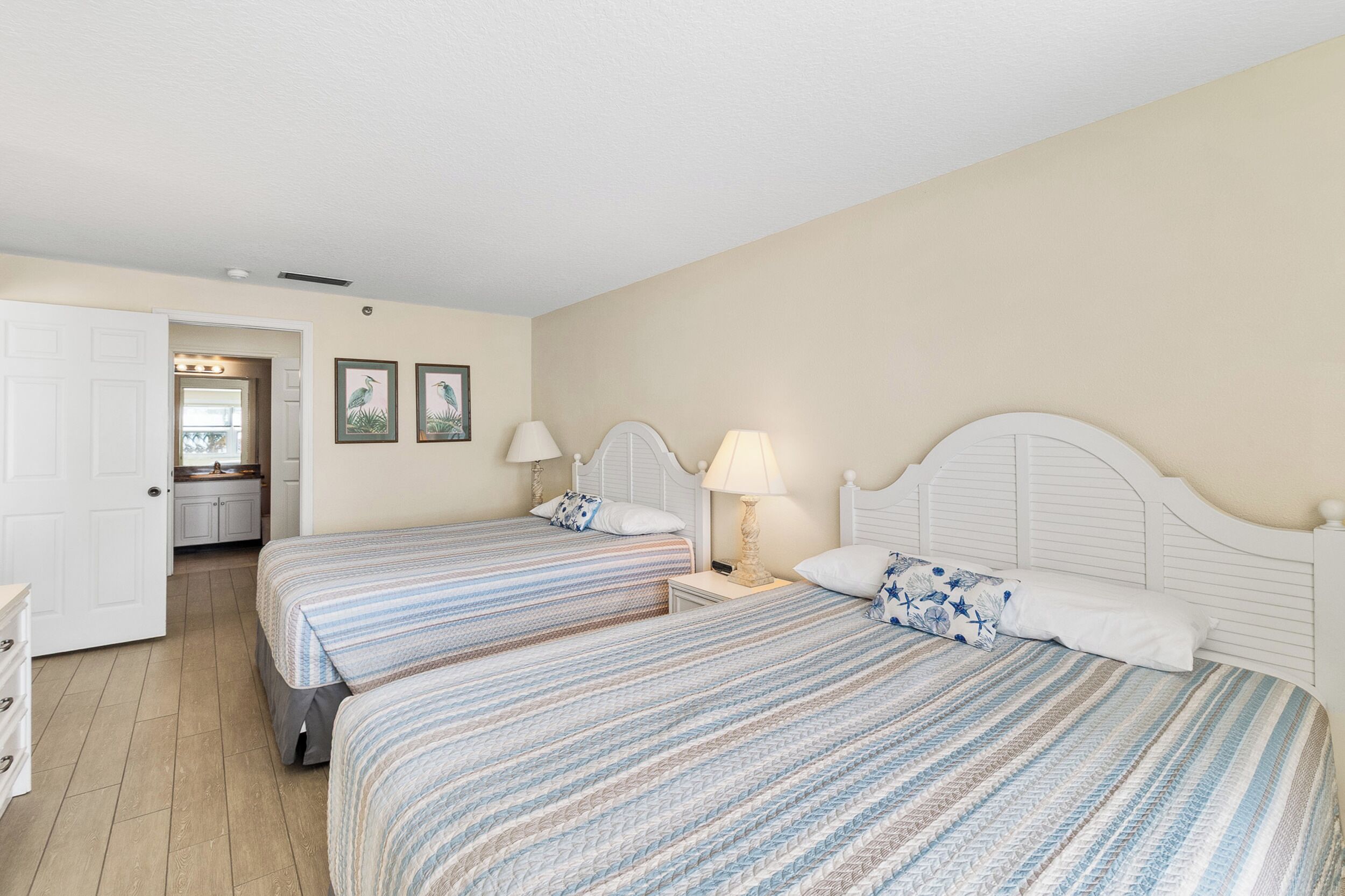Une chambre avec deux lits, une commode blanche et une salle de bain visible à travers une porte ouverte.