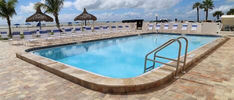 Una piscina con terraza de baldosas, sillas de descanso, palmeras y vista al mar.