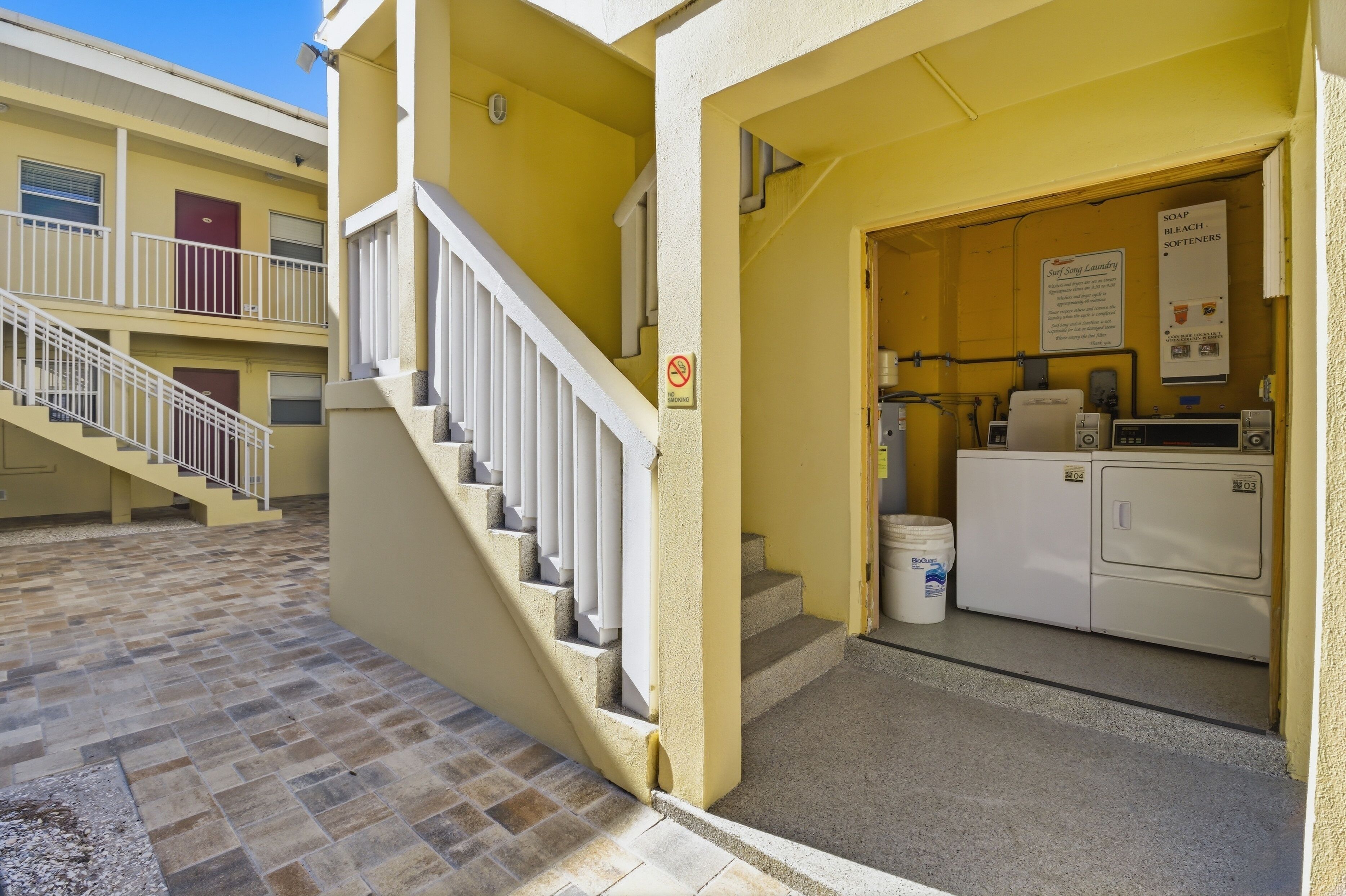 A building with a yellow exterior, a staircase with white railings, and a laundry area with a sign indicating soap, bleach, and softeners.