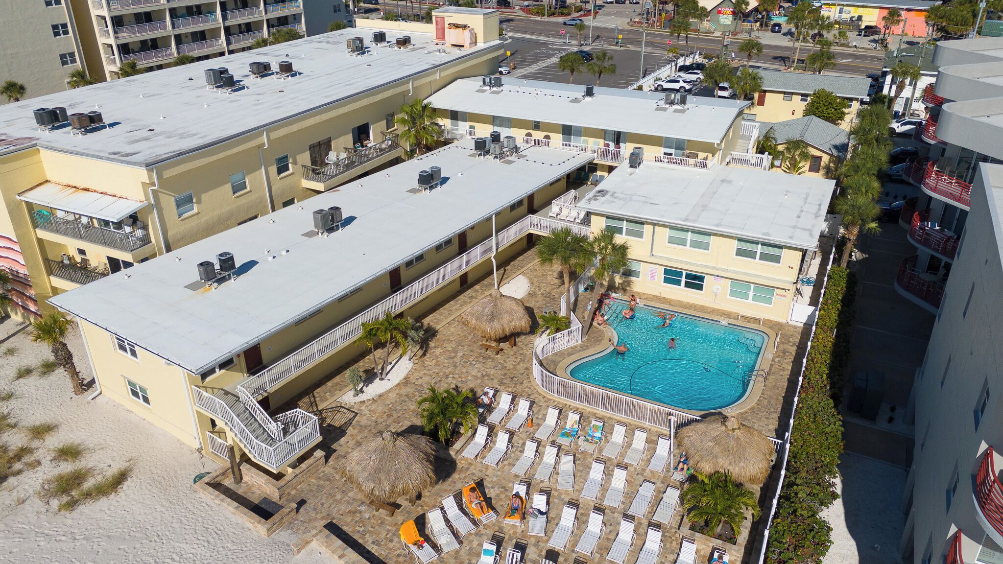 Un hotel de varios pisos con piscina en la azotea, mobiliario exterior y zona de playa.
