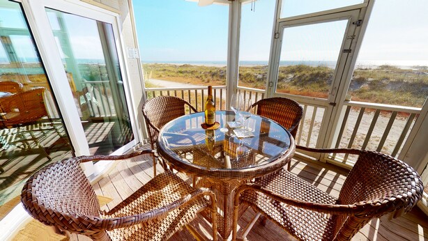 Un balcon vitré, agrémenté de meubles en osier et d’une table, qui offre une vue sur la plage.