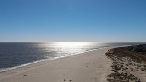 Une plage avec un ciel dégagé, un rivage sablonneux et quelques rochers épars.