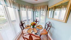 Un coin repas avec une table en verre entourée de chaises, un vase de fleurs et un miroir accroché au mur.