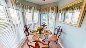 A dining area with a glass table surrounded by chairs, a vase of flowers, and a mirror on the wall.