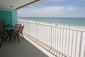 A balcony with a view of a beach, a table with chairs, and a turquoise wall.