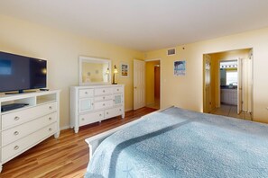 A bedroom with a bed, a dresser, a TV, and a door leading to a bathroom.