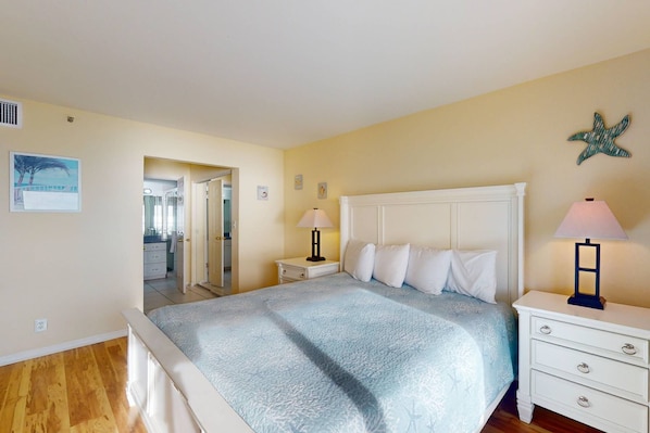 A bedroom with a bed, nightstands, a dresser, and a door leading to another room.