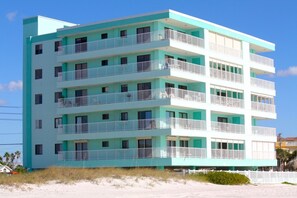 A multi-story building with balconies, located near a sandy area.