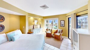 A hotel room with a large bed, a dresser, two wicker chairs, a window with a view of the beach, and a ceiling vent. - Ocean view condo in Wild Dunes (Isle of Palms)