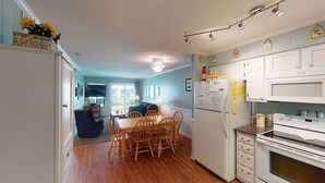 A compact kitchen with white cabinets, a dining table with chairs, and a refrigerator. - Cozy Condo Steps From the Water! (Isle of Palms)