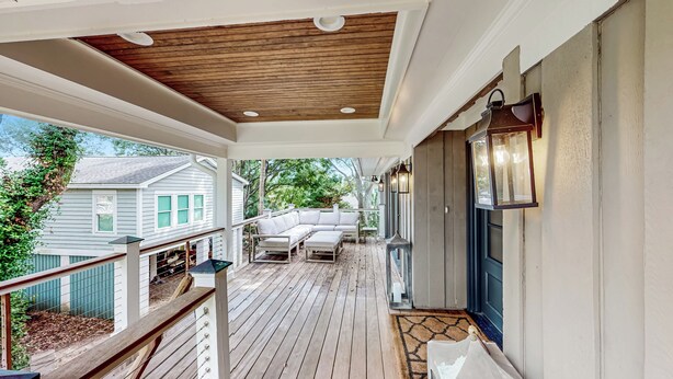 A covered porch with a wooden ceiling, a white sofa, and a small table.
