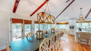 A spacious dining area with a long table, white chairs, and a chandelier.