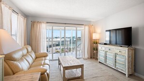 Un salon moderne avec un canapé en cuir, une table basse en bois, un téléviseur posé sur un meuble et un balcon offrant une vue sur la ville.