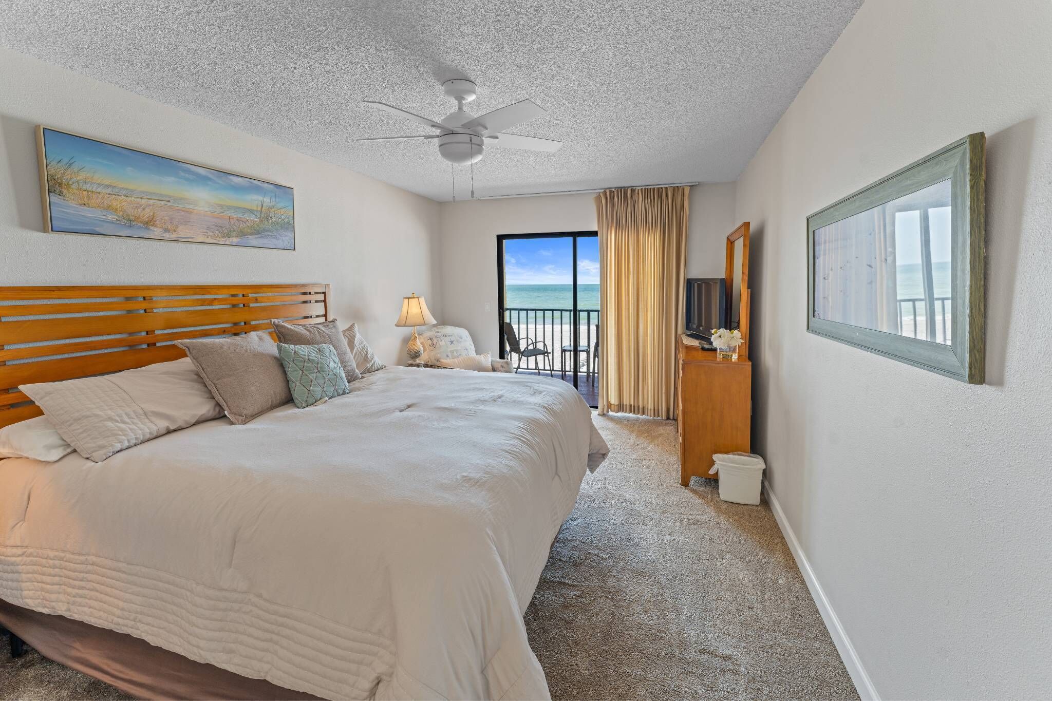 Une chambre d’hôtel avec un grand lit, un ventilateur de plafond, un tableau, une vue sur l’océan et un balcon avec des rideaux.