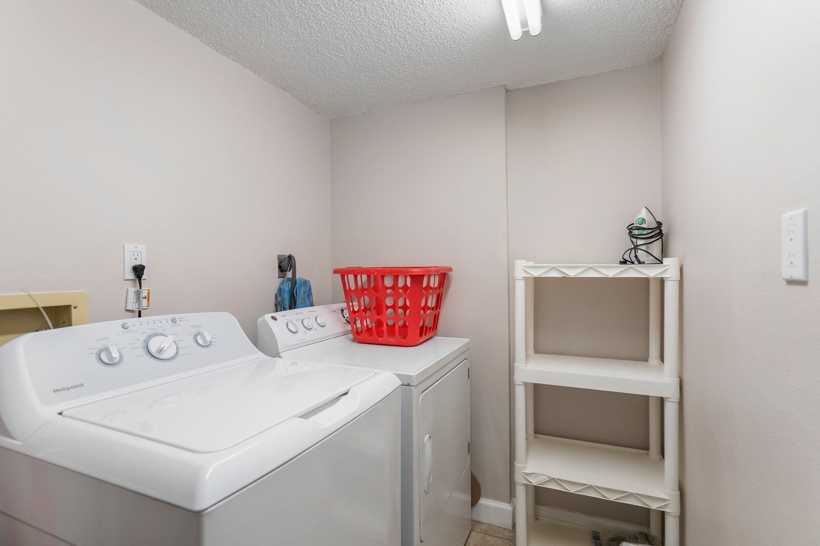 Une buanderie équipée d’un lave-linge et d’un sèche-linge à chargement frontal, d’un panier à linge rouge et d’une étagère blanche.