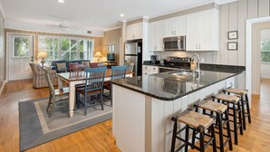 A modern kitchen with a central island, bar stools, and a dining area with a table and chairs. - Walk to beach, screened porch, single level, updated kitchen and baths! (Isle of Palms)