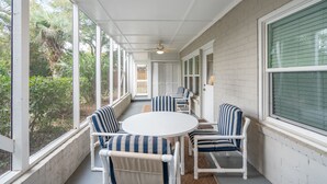 A covered patio with a round table and striped chairs, large windows, and a ceiling fan. - Walk to beach, screened porch, single level, updated kitchen and baths! (Isle of Palms)