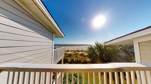 A wooden balcony with a view of the beach and ocean.