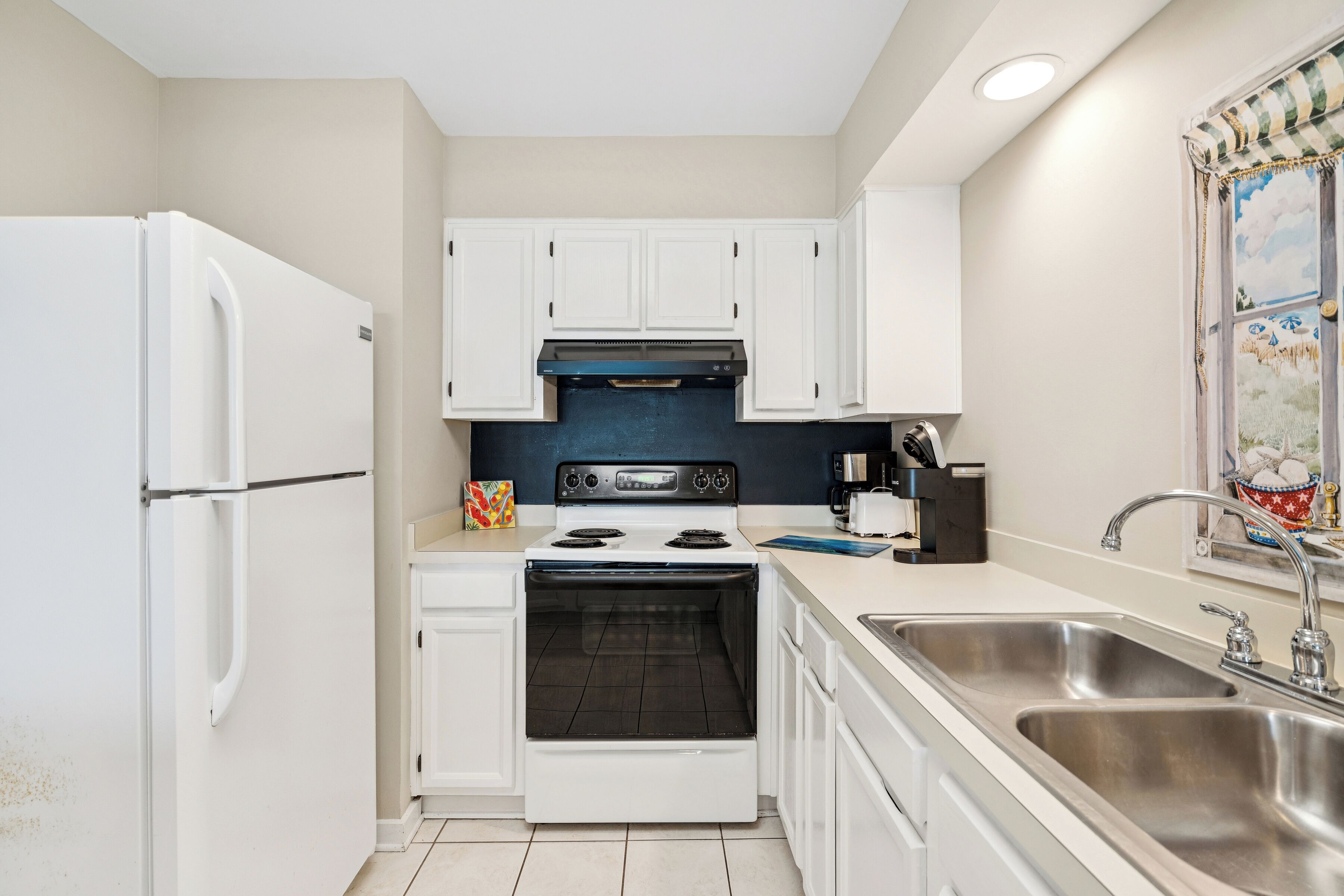 A compact kitchen with white cabinets, a stove, and a sink.