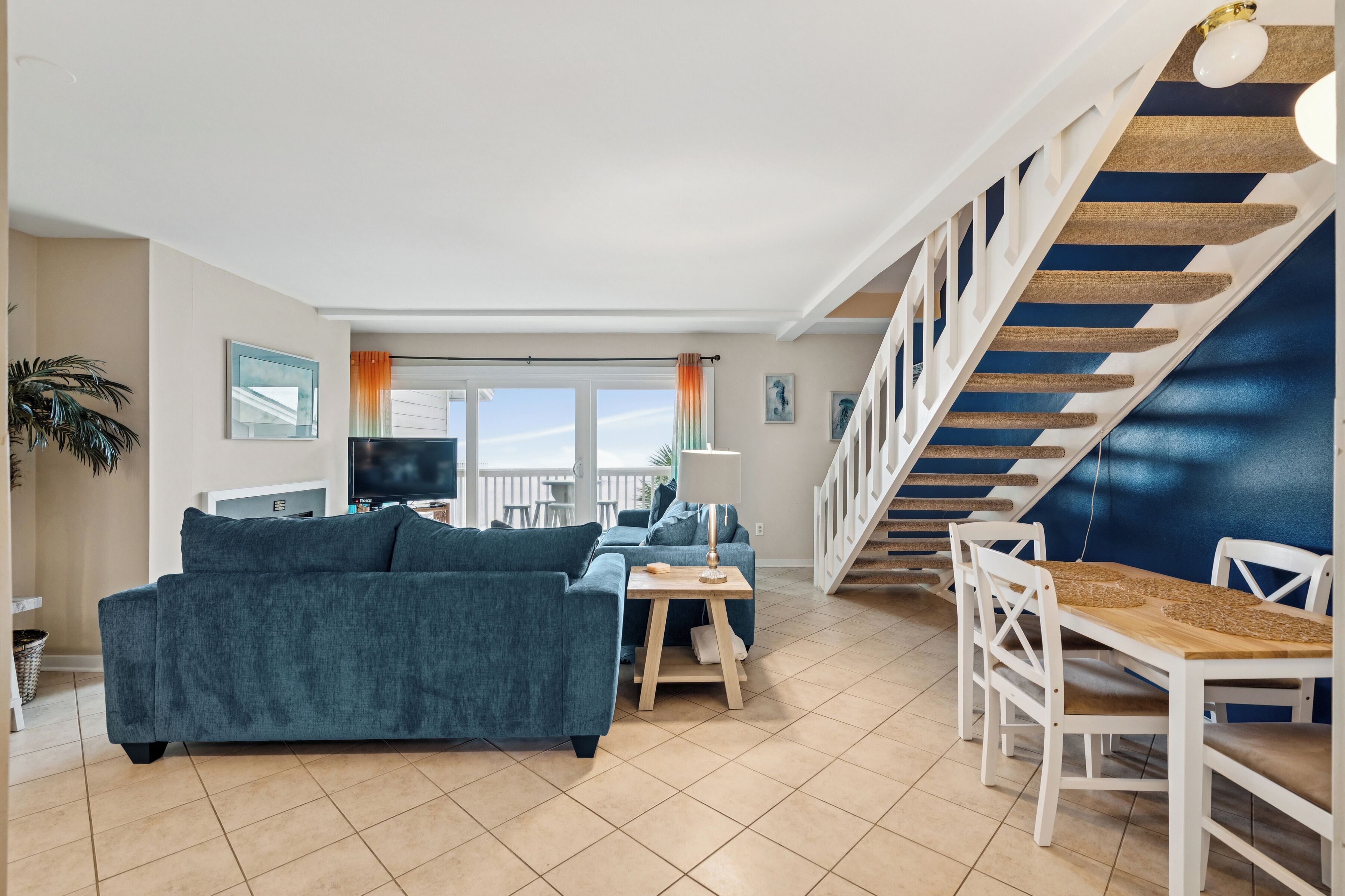 Un vaste espace de vie comprenant un canapé, une table basse et une table à manger avec des chaises. Un escalier, avec un mur d’accent bleu, mène à l’étage supérieur.