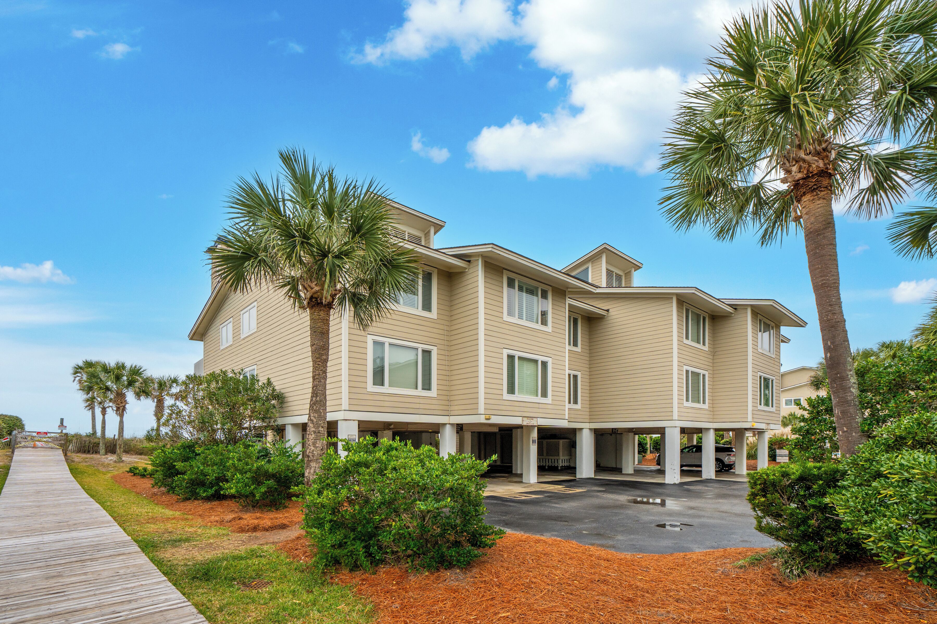 A multi-story hotel with a covered parking area, palm trees, and a wooden walkway.