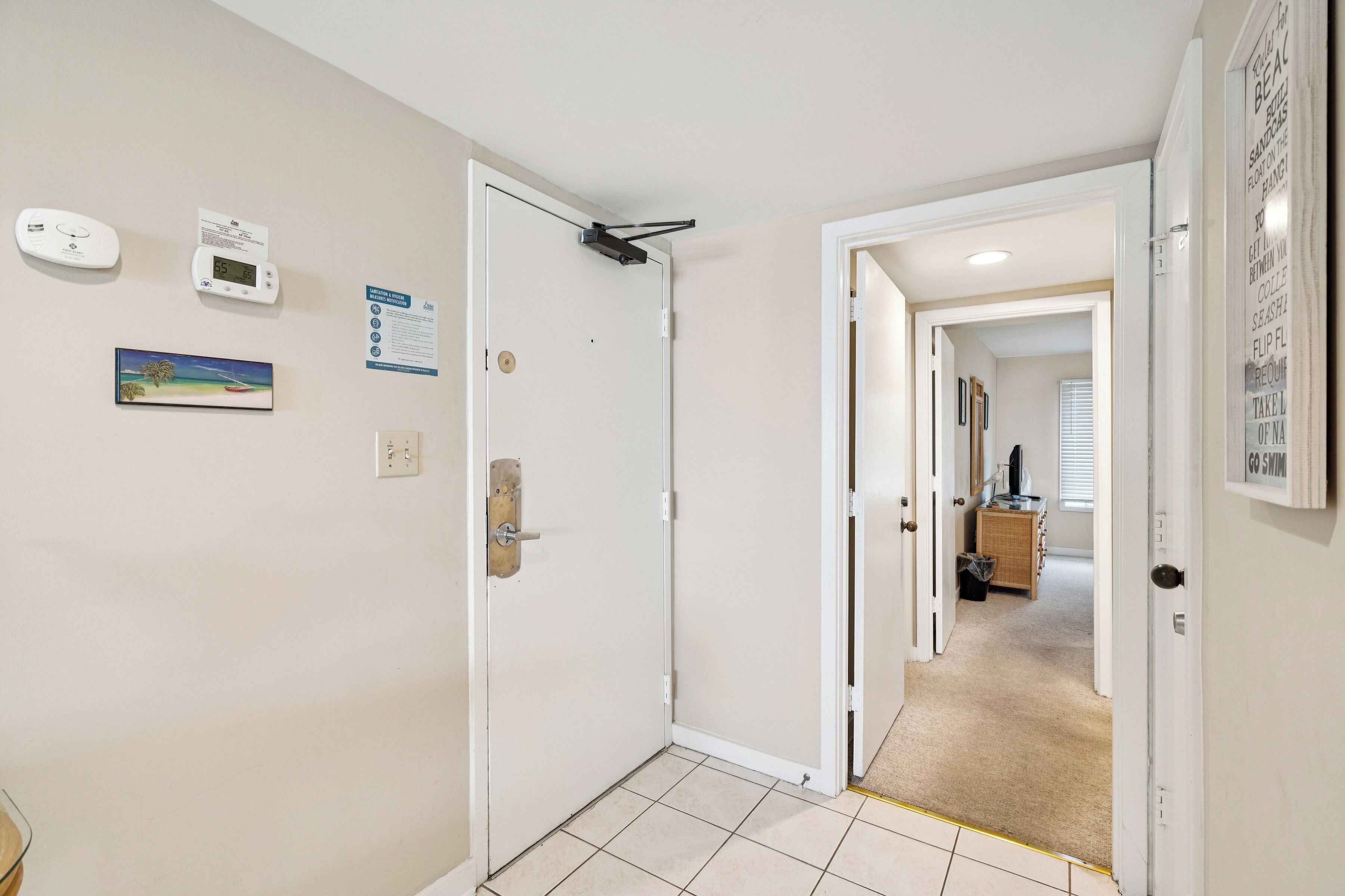 A hallway with a white door, a thermostat, and a framed picture on the wall.