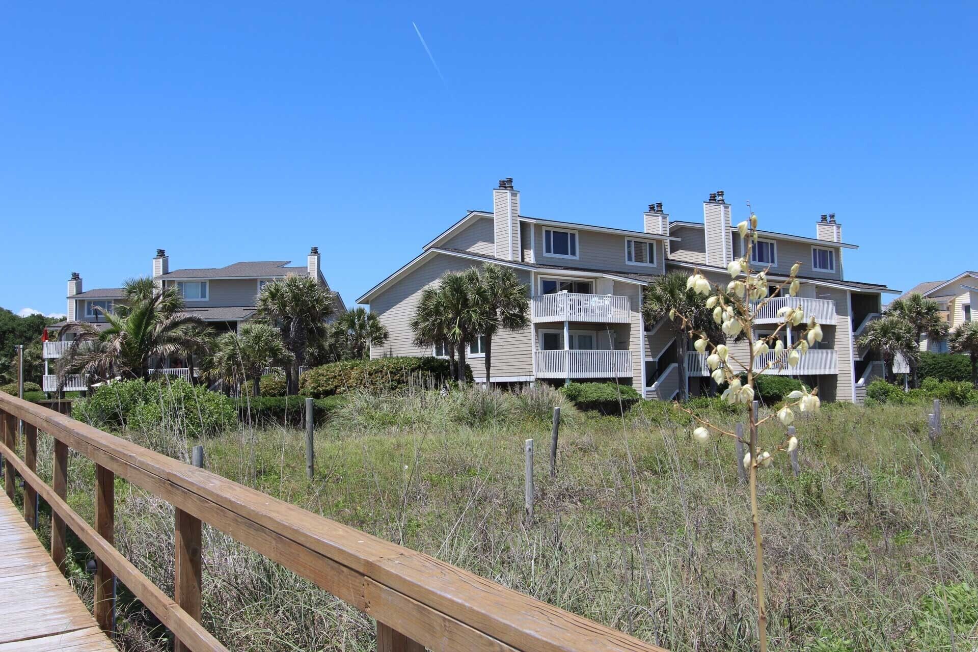 A beachfront property with multiple-story buildings, a wooden boardwalk, and palm trees.
