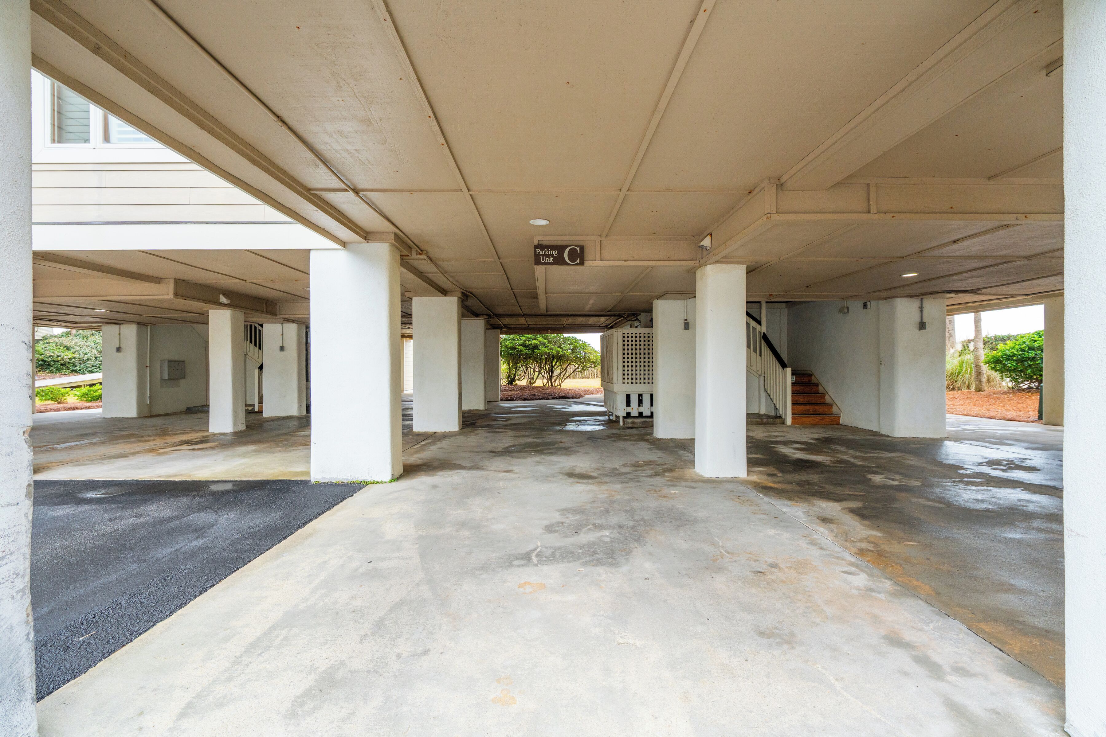 Un parcheggio sotterraneo vuoto con pavimenti e colonne in cemento, una scala e un cartello che indica l'unità di parcheggio C.