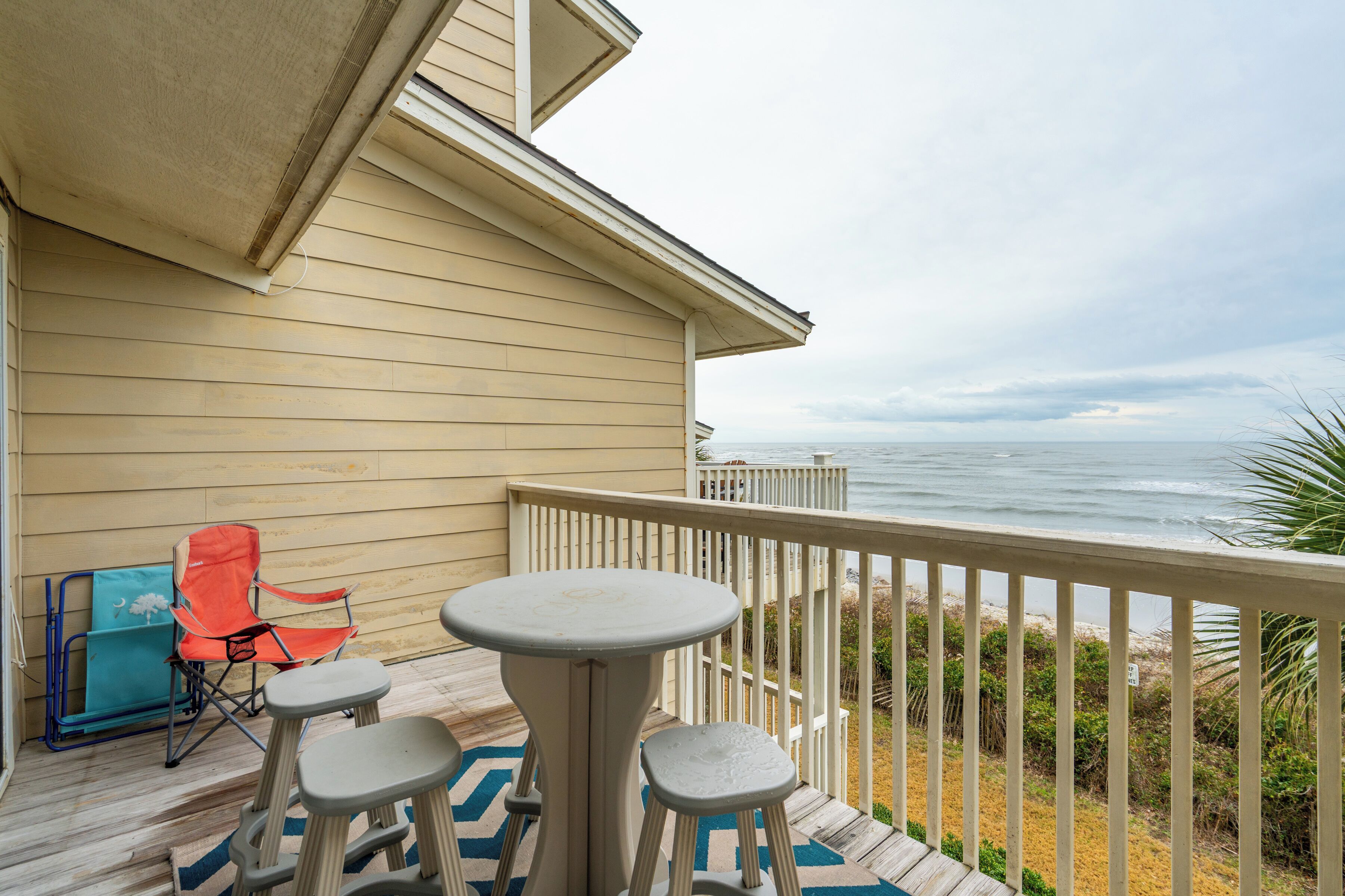 A deck with a table and chairs, overlooking a beach with a railing.