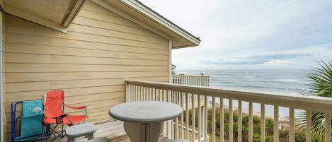 A deck with a table and chairs, overlooking a beach with a railing.