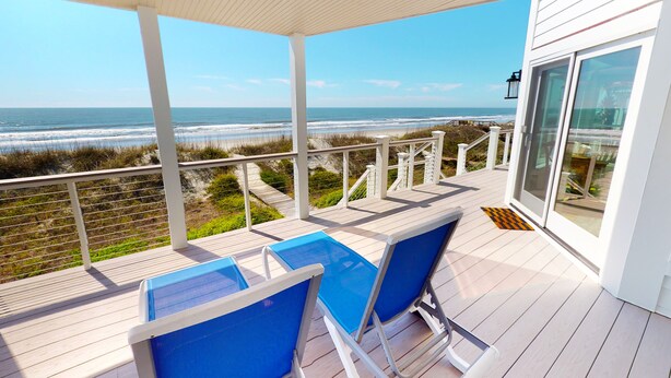 Een balkon met uitzicht op de oceaan, voorzien van blauwe stoelen en een klein zwembad.