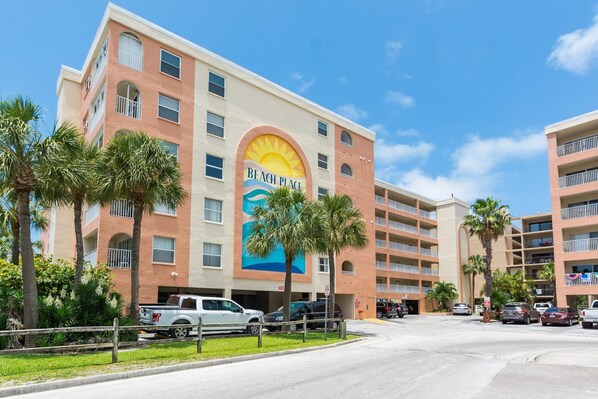 A multi-story hotel with a large sun mural on the facade, palm trees, and a parking lot with several vehicles.