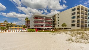 A beachfront hotel with multiple balconies, a sandy beach in the foreground, and palm trees. - Large 1,225 sq ft Unit Beach Views Crimson #204 (Madeira Beach)