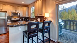 A modern kitchen with granite countertops, stainless steel appliances, and a large island with bar stools. - Crossroads Snowshoe Townhome: Great Views, On Rec Path (Frisco)