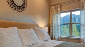 A bedroom with a bed, a bedside table, a mirror, and a window with curtains. - Crossroads Snowshoe Townhome: Great Views, On Rec Path (Frisco)