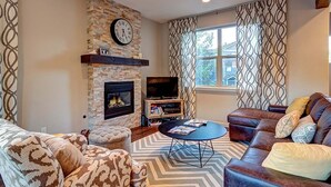 A living room with a stone fireplace, a television, and a patterned curtain. - Crossroads Snowshoe Townhome: Great Views, On Rec Path (Frisco)