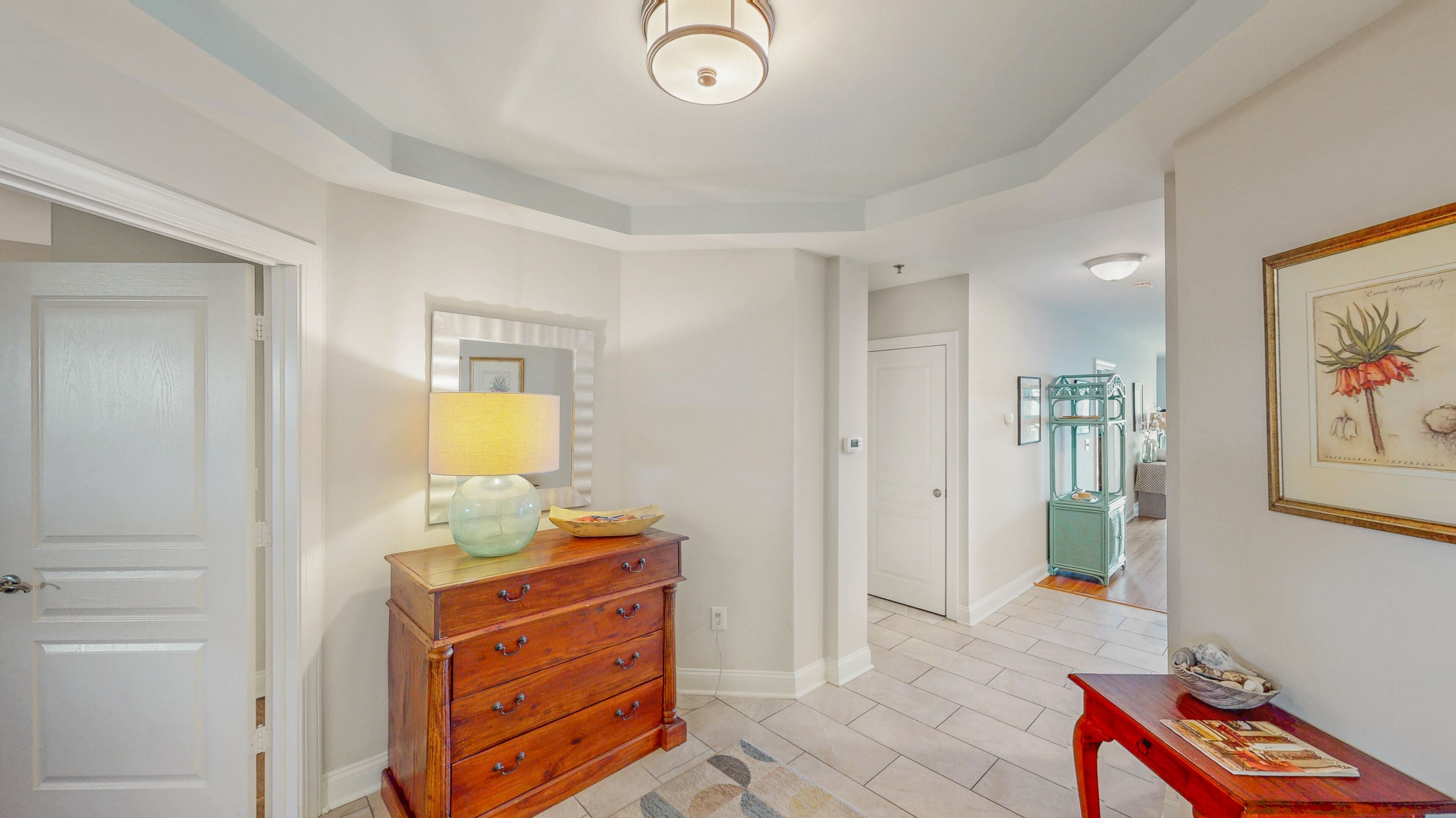 A hallway with a wooden dresser, a lamp, and a framed botanical illustration.