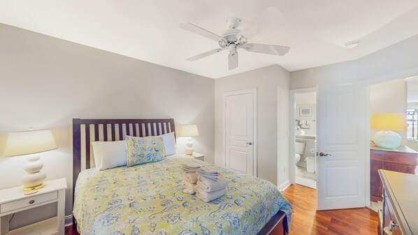 A bedroom with a bed, bedside lamps, a ceiling fan, and a bathroom visible through an open door.