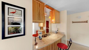 A kitchen with wooden cabinets, a granite countertop, a red chair, and a framed picture of birds. - Great home located near the beach with pool and tennis court access (Isle of Palms)