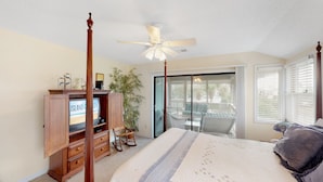 A bedroom with a four-poster bed, a ceiling fan, a television, a sliding glass door to a balcony, and a large potted plant. - Great home located near the beach with pool and tennis court access (Isle of Palms)