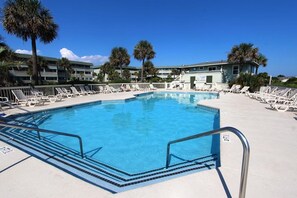 A swimming pool with lounge chairs and palm trees, surrounded by a building with balconies. - Quaint Coastal Hideaway with Beach View! (Isle of Palms)