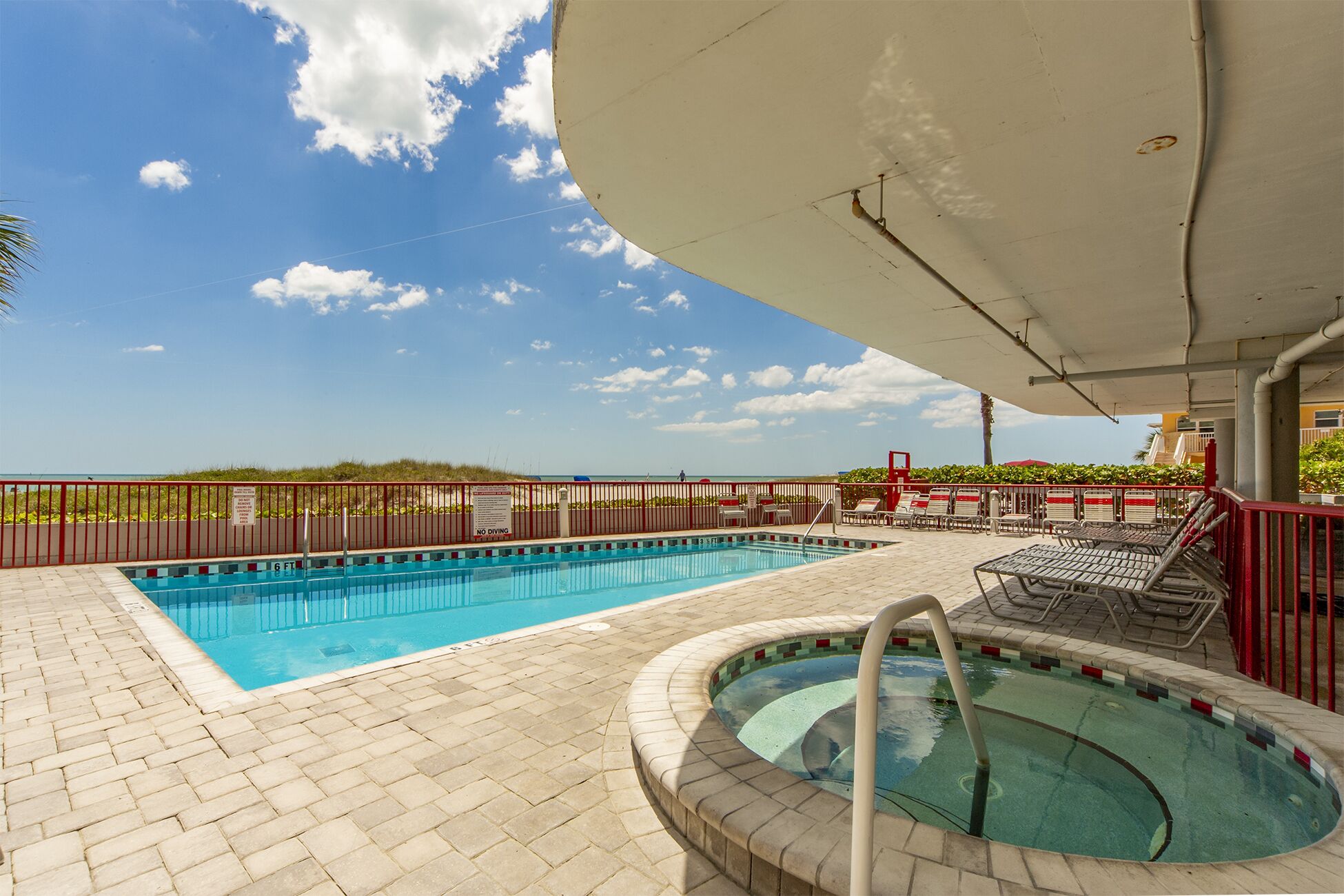 Piscina ao ar livre com hidromassagem, espreguiçadeiras e vista para a praia.