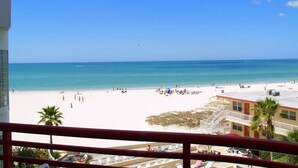Blick auf einen Strand vom Balkon aus, mit blauem Himmel, sandigem Strand und einigen Personen.