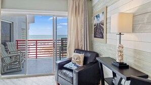 Ein Zimmer mit Balkon, einem Sessel, einem Tisch und einer Lampe.