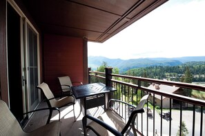 A balcony with wicker chairs and a table, overlooking a mountainous landscape.