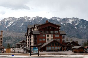 A multi-story hotel with a traditional architectural style, featuring balconies and large windows, set against a backdrop of snow-capped mountains.